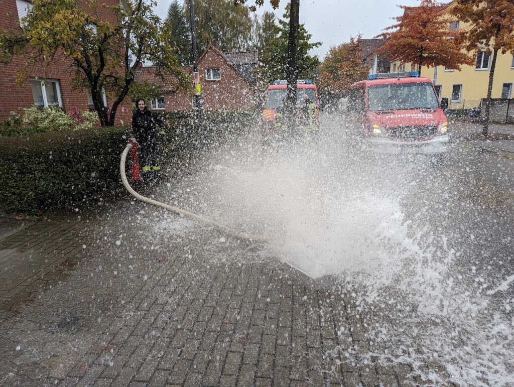 Ein Hydrant wird gespült mit der Hilfe eines Spülkastens. Das Wasser spritzt kontrolliert aus dem Spülkasten, doch aufgrund des hohen Drucks ist es Fontänenartig.